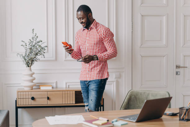 istock Confident handsome african american businessman using mobile, standing in office during working day 1400396104