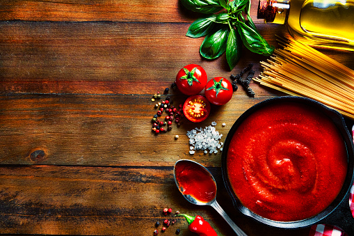 Table top view of ingredients to prepare pasta and tomato sauce in a domestic rustic kitchen with copy space