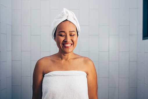 Portrait of a young Asian woman after a shower in her bathroom, smiling with her eyes closed.
