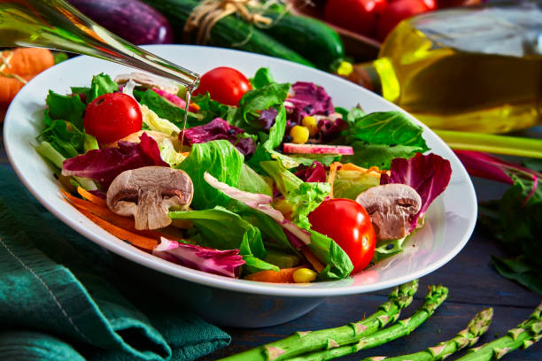 Vegan food themes. Close-up of pouring olive oil on spring salad on rustic wood table Vegan food themes. High angle view of a colorful spring salad on rustic white wood table. Included ingredients: Olive oil, peppermint, chia, tomatoes, broccoli, lettuce, bell peppers, mushroom, carrots, radicchio and almonds. salad fruit lettuce spring stock pictures, royalty-free photos & images