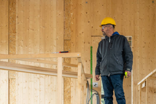 Building contractor in wooden house room. Modern family home construction. Worker in yellow protective helmet holding measuring tape