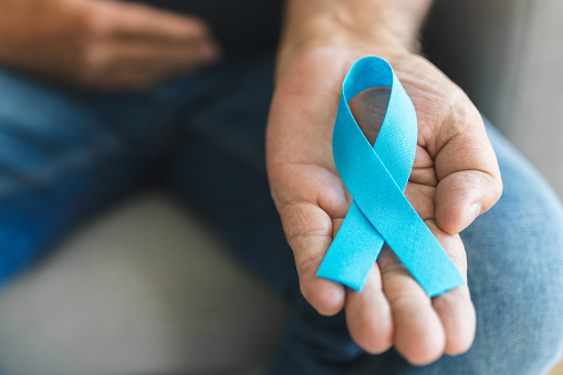 Senior man holding a blue cancer awareness ribbon in hand