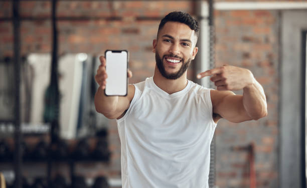 istock Fit young man showing his smartphone screen. Muscular bodybuilder using a smartphone in the gym. Young athlete using an online app on his cellphone. Athletic man using his mobile device 1400409076