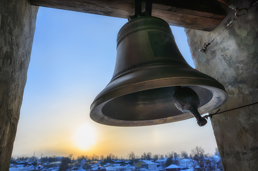 Campana de fundición pesada en el campanario de la iglesia contra el cielo amarillo-azul del atardecer en la abertura de la ventana. Primer plano. photo
