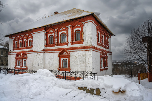 Ancient majestic Voivode House in the historical part of Solikamsk (Northern Ural, Russia) in winter. Close-up. Traditional white and red ancient style and patterned masonry windows. embossed gray sky