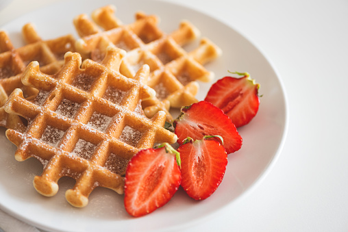 Belgian waffles with strawberry and powdered sugar on white plate. Breakfast food concept. Copy space