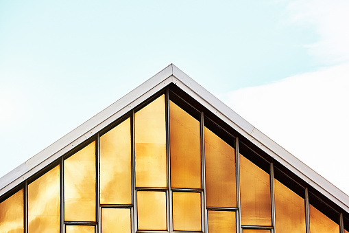 Church building with windows covered in film material that shines in beautiful gold color as it reflects the sky.