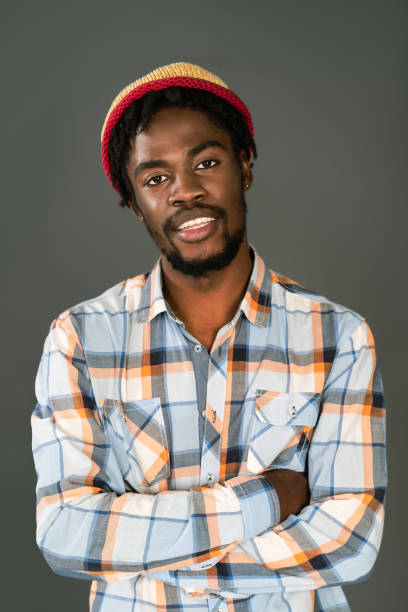 istock Young smiling black man in afro hat standing with arms folded looking at camera. Cheerful african american young man in plaid shirt looking at camera isolated on gray background 1400416191