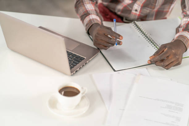 istock Top view, young african student man making notes working at home while enjoying cup of coffee with smartphone next to him. African student study using laptop while coffee break at campus 1400416221
