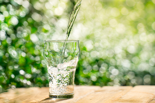 Pour water from a plastic bottle into a glass. The background of the plants in the garden. soft focus.