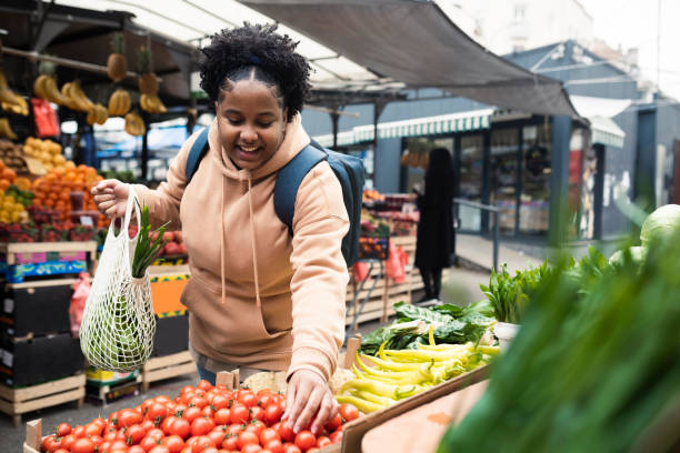 市場で野菜を買うアフリカ系アメリカ人の若い女性 - spending money adult african ethnicity bag ストックフォトと画像