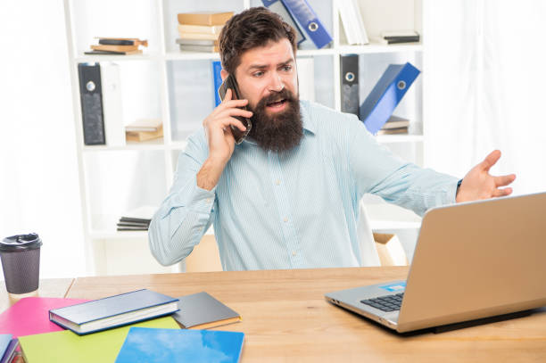 istock Stressed manager yelling on mobile phone working on laptop in office, stress 1400417747