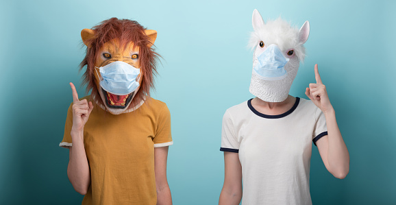 Young woman wearing lion and alpaca and protection medical mask pointing up with index finger, capture the attention or warning advice