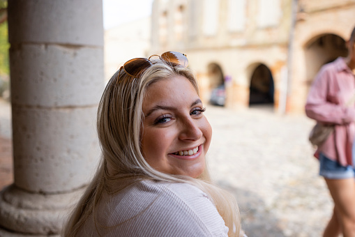 A cheerful smiling portrait of a young blonde woman looking over her shoulder and smiling and loking to the camera as she enjoys a trip to Auvillar which is a small village in Toulouse in the South of France.