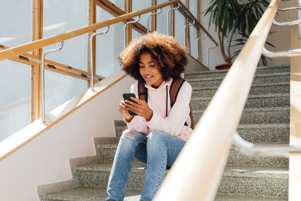 istock Smiling female student with backpack sitting on stairs and using mobile phone 1400419434