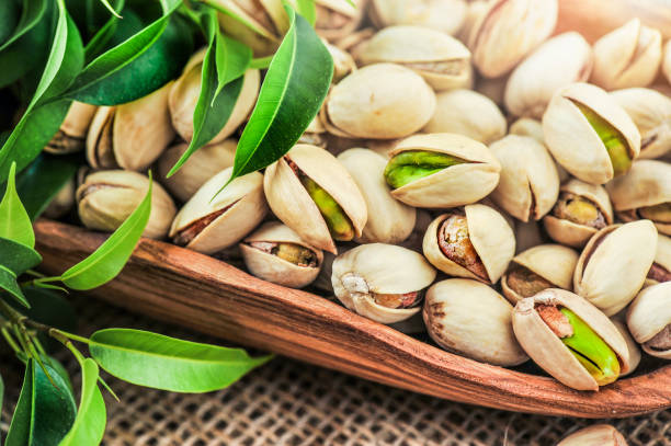Bowl with pistachios nut on a wooden table with green leaves. Bowl with pistachios nut on a wooden table with green leaves. Pistachio nuts detail.. Pistachio stock pictures, royalty-free photos & images