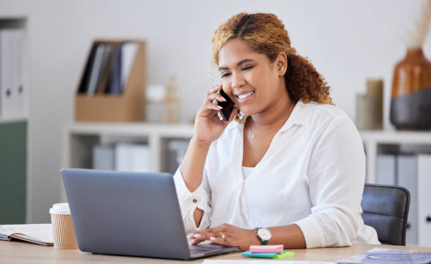 istock Mixed race businesswoman on a call using a phone while working on a laptop alone at work. One hispanic businesswoman talking on a cellphone while working on a computer at a desk in an office 1400421935