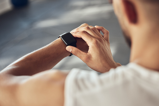 Fit athlete tracking his progress on his watch. Strong athlete using his smartwatch in the gym. Bodybuilder checking the time on his watch. Muscular man timing his workout in the gym