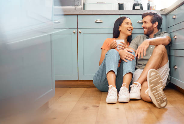 istock Young happy interracial couple bonding while drinking coffee together at home. Loving caucasian boyfriend and girlfriend sitting on the kitchen floor. Cheerful husband and wife relaxing and spending time together 1400424176