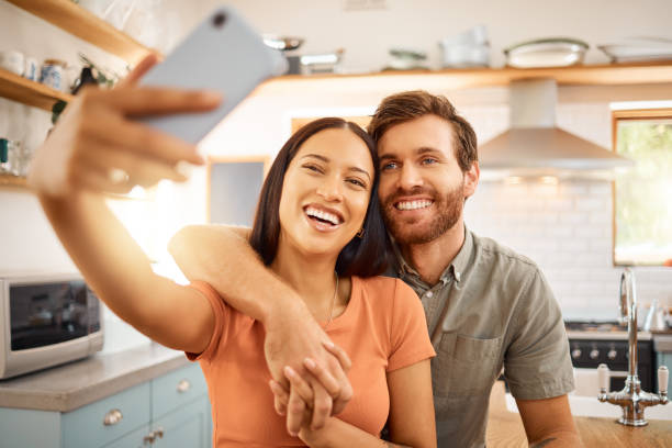 istock Young content interracial couple taking a selfie with a phone together at home. Joyful mixed race girlfriend taking a photo with her caucasian boyfriend on a cellphone. Happy husband and wife relaxing and spending time together in the morning 1400425018