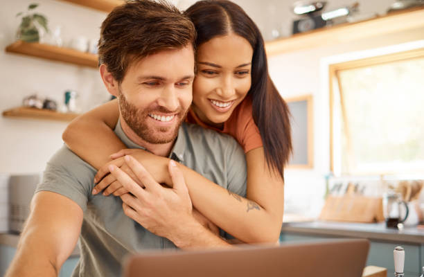 istock Young happy interracial couple bonding while using a laptop together at home. Caucasian boyfriend and girlfriend looking at a computer screen. Cheerful husband and wife working on a laptop together 1400426369