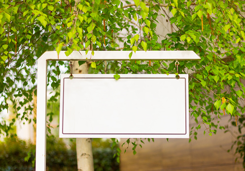 blank white metal hanging signboard on the street among the trees with copy space. place for text, template, mock up