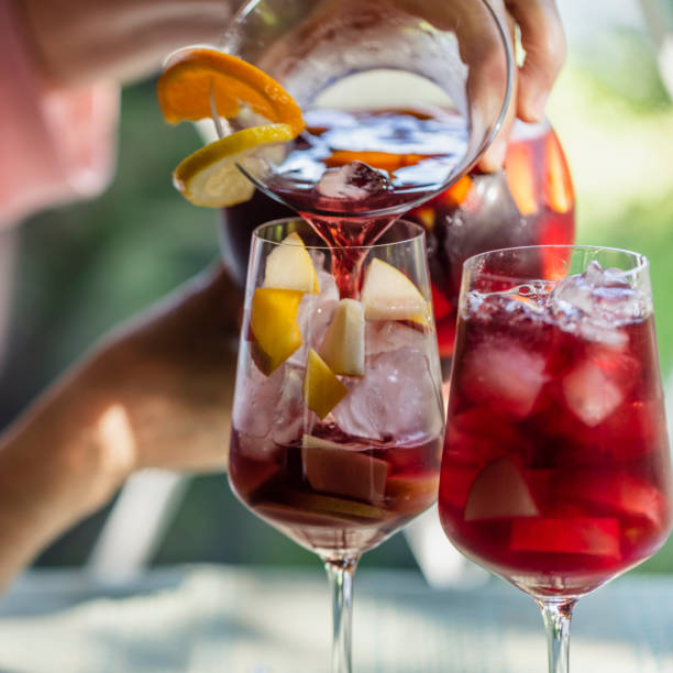 Sangria Time! During a photo shoot, a senior woman is pouring some Sangria in wine glasses. sangria stock pictures, royalty-free photos & images