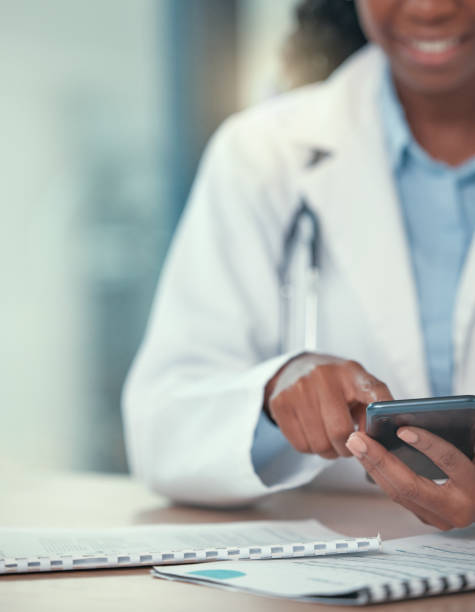 African american doctor using their smartphone. Medical professional sending a text on their cellphone. Closeup on hands of medical professional browsing an app online using a mobile phone African american doctor using their smartphone. Medical professional sending a text on their cellphone. Closeup on hands of medical professional browsing an app online using a mobile phone health technology photos stock pictures, royalty-free photos & images