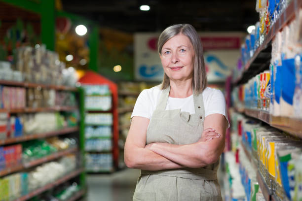 Portrait of happy senior woman grocery store employee with arms crossed smiling and looking at camera Portrait of happy senior woman grocery store employee with arms crossed smiling and looking at camera small business saturday stock pictures, royalty-free photos & images