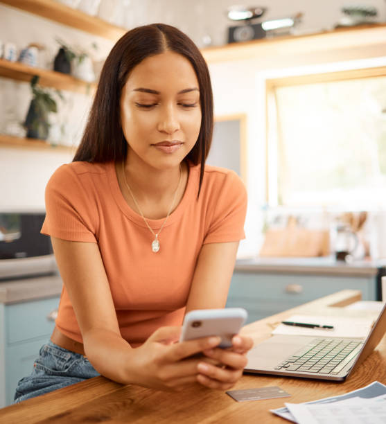 istock Young beautiful happy mixed race businesswoman holding and using a phone while working from home. One content hispanic woman using social media on her cellphone while using a laptop 1400435772