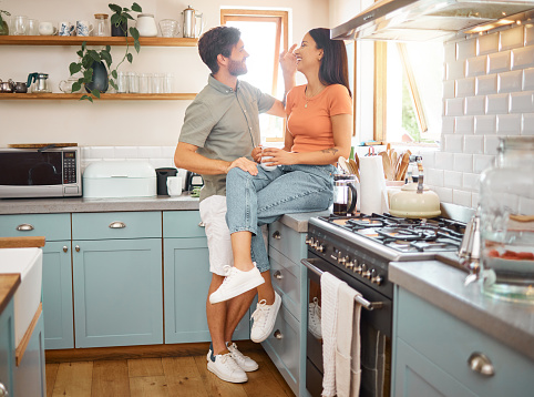 Young cheerful interracial couple bonding while drinking tea together at home. Loving caucasian boyfriend and mixed race girlfriend standing in the kitchen. Content husband and wife relaxing and spending time together in the morning
