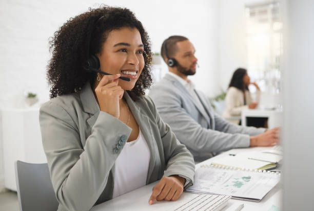 istock Young cheerful mixed race female call center agent answering calls while wearing a headset at work. Hispanic businesswoman with a curly afro talking on a call while working on a desktop computer at a desk in an office 1400436486