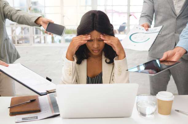 istock Young african american businesswoman suffering from a headache while using a laptop and working in a demanding environment. Stressed businessperson looking tired while working with a group of colleagues at work 1400436494