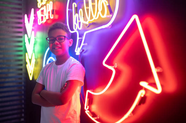 Waist-up portrait of a happy teenage boy in trendy spectacles posing for the camera in a nightclub