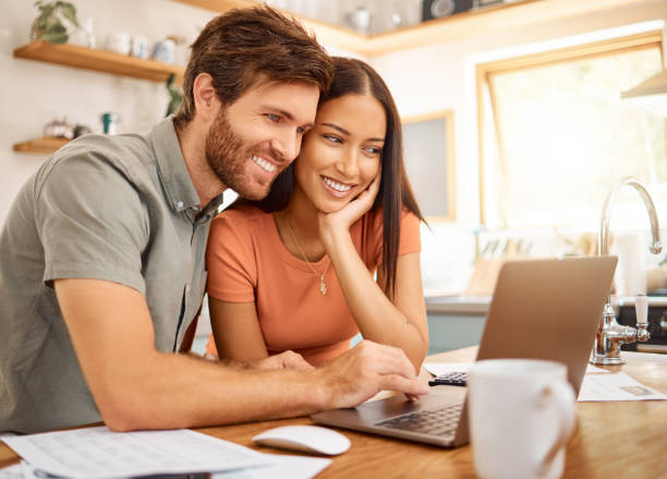 istock Young cheerful interracial couple bonding while typing on a laptop together at home. Caucasian boyfriend and girlfriend working through their bills and using a laptop. Cheerful husband and wife browsing online on a computer 1400436730
