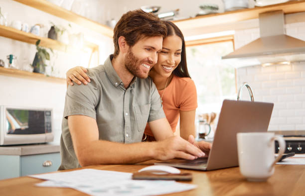 istock Young cheerful interracial couple bonding while working on a laptop together at home. Caucasian boyfriend and girlfriend working through their bills and using a laptop. Content wife and husband browsing online on a computer 1400436733