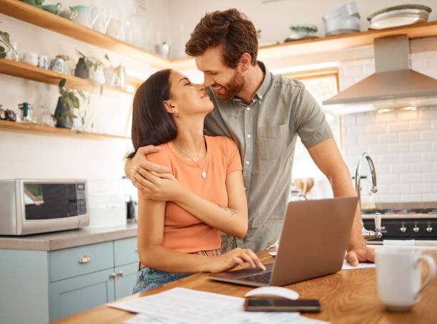 istock Young happy interracial couple bonding while going through paper and using a laptop together at home. Caucasian boyfriend and girlfriend hugging in the kitchen. Cheerful husband and wife working on a laptop together 1400437298