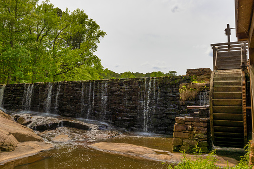 Raleigh, North Carolina, USA - May 1, 2022:  Water wheel and dam with water spilling over it at Yates Mill