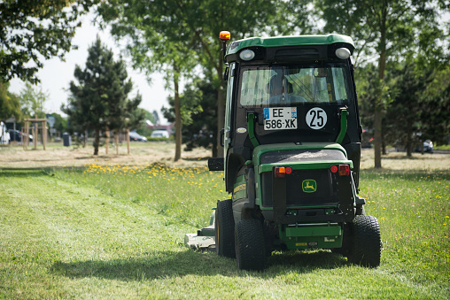 Mulhouse - France - 31 May 2022 - municipal employee driving green tractor and lawn mower, shears lawns in urban park