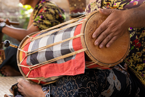 A musician plays a kendhang or ketipung, a traditional Balinese instrument, as part of a musical ensemble or gamelan, during a performance