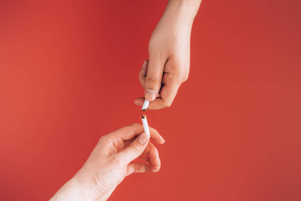 One person takes cigarette from another against red background stock photo
