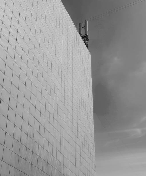 Black-and-white photo The exterior wall of a modern commercial-style building, paneled with tiles, on the roof modern antennas against the sky stock photo