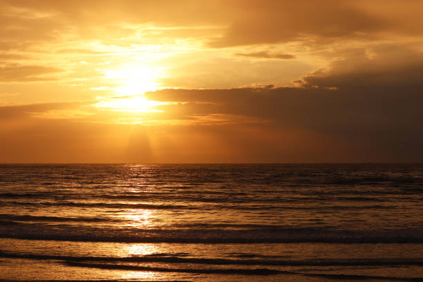 istock Sunset on a beach, orange sun is shining through the clouds and reflected in dark waves 1400448101