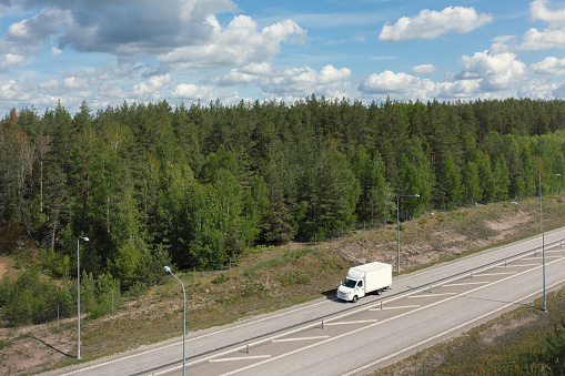 Aerial view of a delivery truck travelling on a highway through a forest landscape.