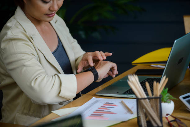 bizneswoman sprawdzająca czas i patrząca na inteligentny zegarek na rękę w domowym biurze.  azjatka widząc zegar do pracy. biurko z laptopem, raport roczny i podsumowujący. czas na spotkanie na spotkanie. - checking the time time clock women zdjęcia i obrazy z banku zdjęć