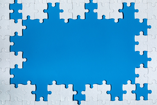 Framing in the form of a rectangle, made of a white jigsaw puzzle. Frame text and jigsaw puzzles. Frame made of jigsaw puzzle pieces on blue background.