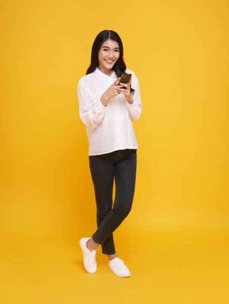 istock Happy young Asian woman using mobile phone isolated over yellow background. 1400451879
