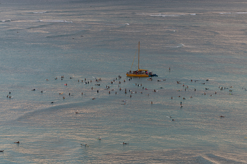 Oahu, USA - Nov 7, 2021: Late in the day surfers and a sail boat navigating through the crowd off Waikiki beach.