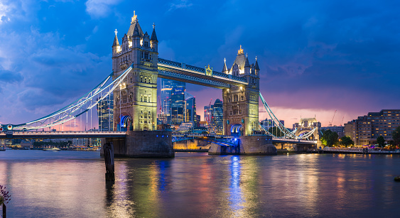 The iconic gothic battlements of Tower Bridge framing the modern skyscraper skyline of the City of London illuminated against a dramatic sunset sky over the River Thames in the heart of the UK’s vibrant capital city.