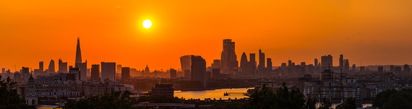 Orange sun setting over the iconic skyscraper skyline of central London and the River Thames, UK.